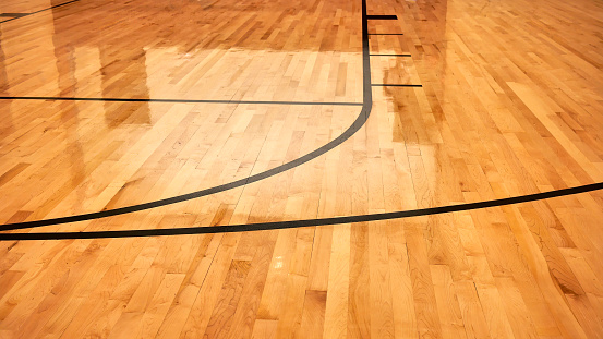 Interior de la cancha deportiva cubierta de baloncesto moderna vacía, piso de madera con revestimiento semibrillante, luces artificiales reflejadas photo