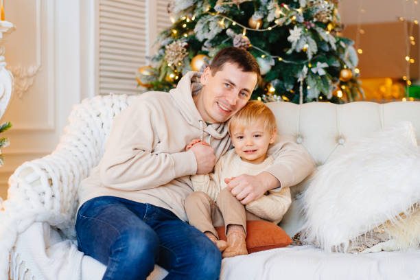 istock happy dad with his young son on the couch by the Christmas tree. 1452308434