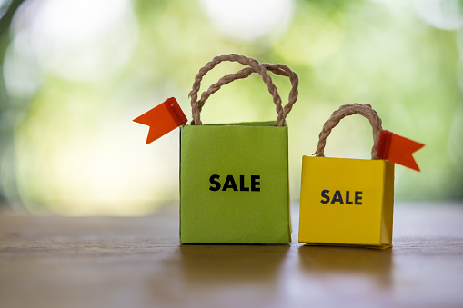 Miniature paper shopping bags with sale word on wood table and against nature background. Shopping day concept. Black friday creative idea concept