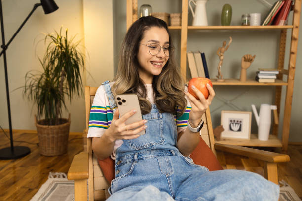 istock Girl enjoying an apple at home and using smartphone 1452316516