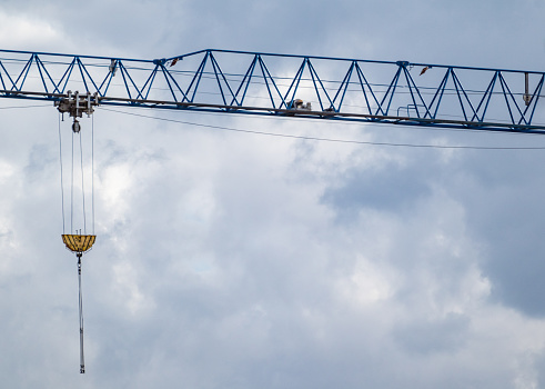 Blue tall crane projecting arm for lifting heavy weights on construction site on cloudy scenic sky background