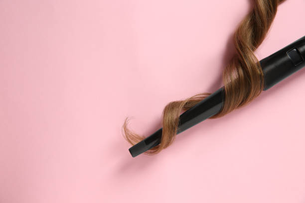 ピンクの背景に現代のクリップレスヘアアイロンと茶色のヘアロック、上面図。テキスト用のスペース