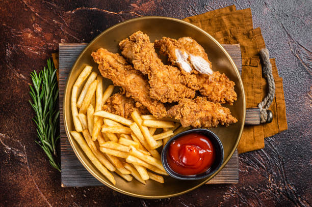 tiras tiernas de pollo empanizado frito con papas fritas y ketchup de tomate en un plato. espalda oscura. vista superior - crispy fotografías e imágenes de stock