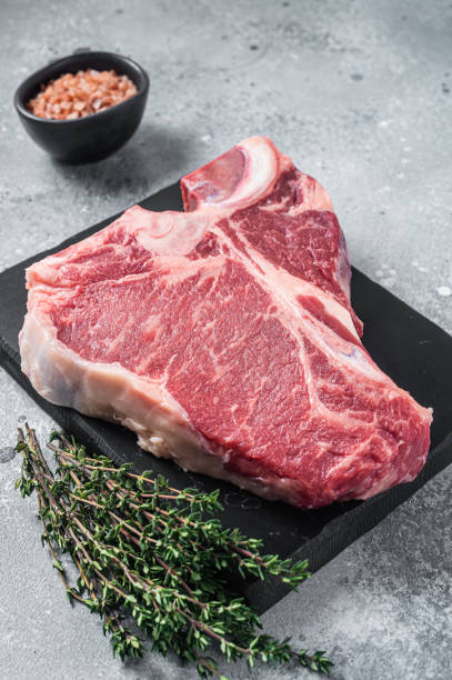 Raw dry aged wagyu porterhouse beef steak, uncooked T-bone on marble board with thyme. Gray background. Top view Raw dry aged wagyu porterhouse beef steak, uncooked T-bone on marble board with thyme. Gray background. Top view. t bone steak stock pictures, royalty-free photos & images