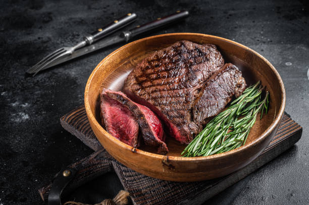 bbq grilled medium rare top sirloin beef steak, rump steak in a wooden plate. black background. top view - circular skirt fotos imagens e fotografias de stock