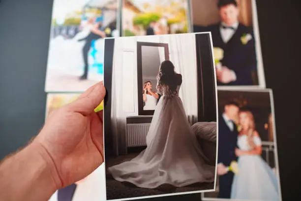 Photo of printed wedding photos on a black background and in hand.