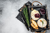 Grilled Camembert Brie cheese with a cranberry sauce, toast and rosemary in a wooden tray. White background. Top view. Copy space