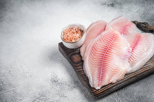 istock Uncooked tilapia fish fillet on a wooden board. White background. Top view. Copy space 1452326050