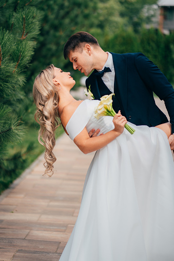 stylish newlyweds. the groom in a bow tie and the blonde bride in traditional wedding clothes dance in a park. wedding fashion and organization of a holiday in the summer in the fresh air.
