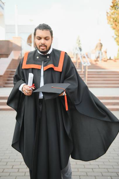 istock Indian graduate in graduation robe with diploma in university campus copy space. 1452335943