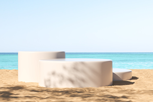 White cylinder platform on sand beach with sea view, abstract shadow. Mockup for product display and promotion. 3D rendering