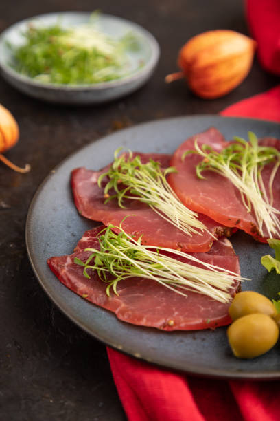 istock Slices of smoked salted meat with cilantro microgreen on black. Side view, selective focus. 1452337209