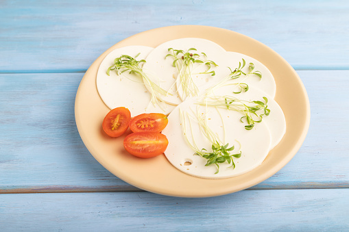 White cheese with tomatoes and cilantro microgreen on blue wooden background. side view, close up.