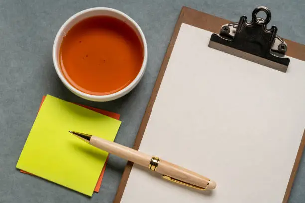 clipboard with a blank paper, desktop flat lay with a cup of tea, sticky notes and a stylish pen