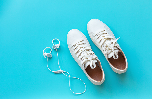 White classical leather shoes and earphones on blue background. Still life, modern shoes. minimalistic background