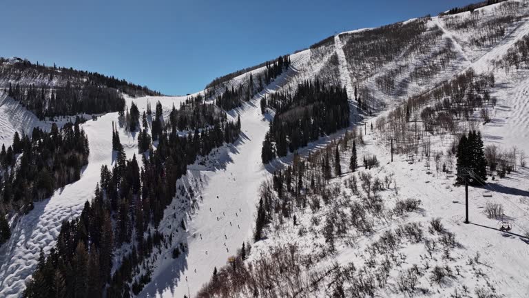 Park City Utah Aerial v2 low level flyover mountain ski slopes up to the top capturing downhill skiers and uphill cableway lift during winter on a sunny day - Shot with Mavic 3 Cine - February 2022