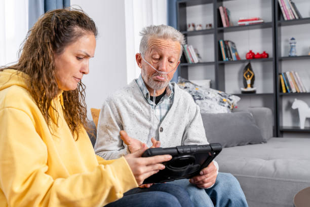 un homme âgé prend l’aide d’une jeune femme sur tablette numérique - grandparent senior adult child reading photos et images de collection