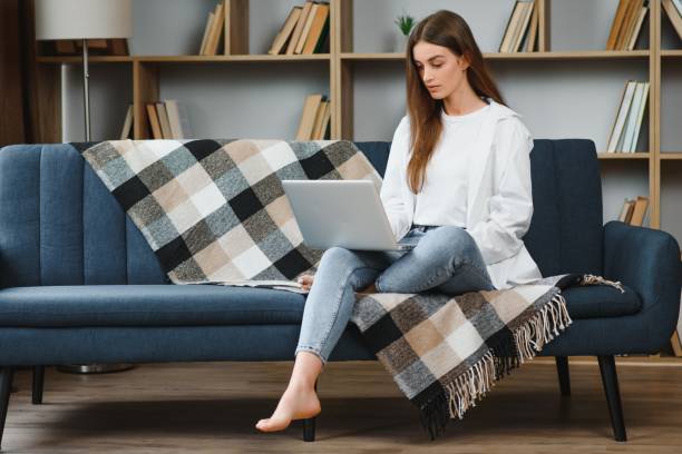 istock Smiling attractive young woman sitting on sofa using laptop communicating working online at home, happy teen girl typing on computer, enjoying writing blog or chatting with friends in social network 1452352949