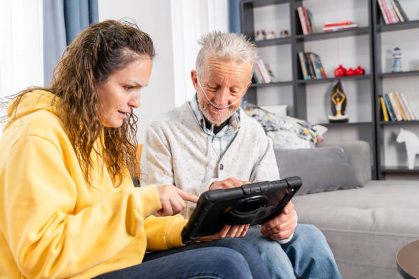 un homme âgé prend l’aide d’une jeune femme sur tablette numérique - grandparent senior adult child reading photos et images de collection