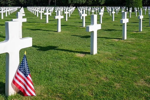 An American flag standing at the gravestone of a killed soldier at the war cemetery in Normandy