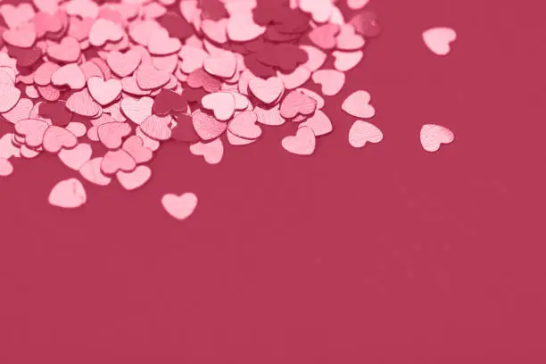 Festive background with magenta metallic heart shaped confetti. Copy space for your text. Selective focus. Color trend year 2023.