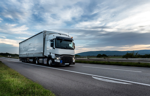 Big White truck driving on the highway through countryside landscape at sunset.