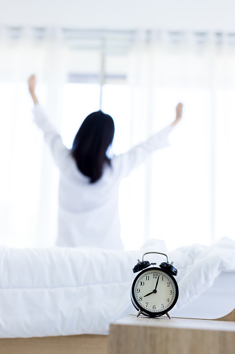 Alarm clock that is going to ring a in morning on background of woman in bed.  Alarm clock  a good day with background happy woman stretching in bed after waking up