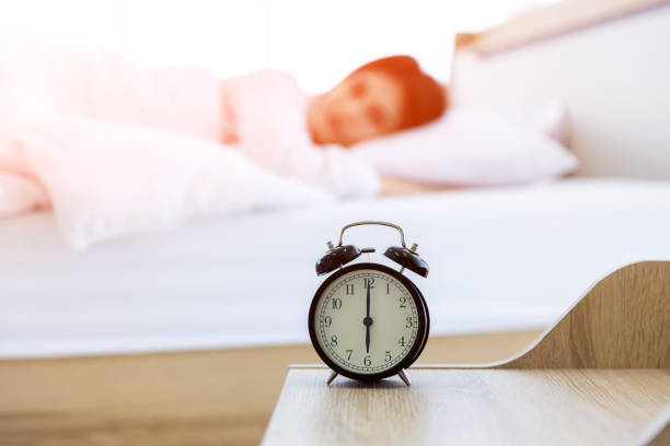 despertador que vai tocar uma manhã no fundo da mulher na cama. despertador na mesa de cama lateral que vai tocar de manhã cedo para acordar a mulher na cama dormindo fundo. - period costume fotos - fotografias e filmes do acervo