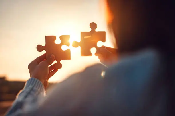Closeup hands of woman connecting jigsaw puzzle with sunlight effect, Jigsaw alone wooden puzzle against sunset, Business solutions, Success and strategy concept