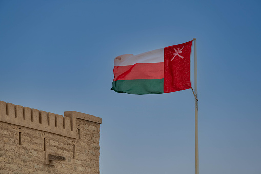 The flag of Oman flying from a flagpole with the crenellations of Mirbat castle visible