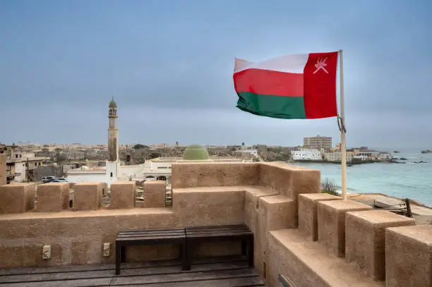 The flag of Oman flying from a flagpole on the crenelated roof of Mirbat Fort