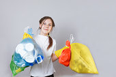 girl in protective rubber yellow gloves holds four multi-colored bags with sorted garbage for further processing