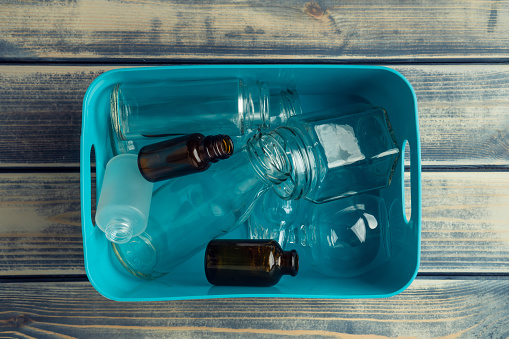 Blue plastic square box full of transparent plastic and glass bottles on wooden background. Sustainable development, recycling and sort. Nondegradable rubbish and environmental crisis. Top view