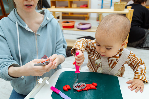 Mother teaching toddler to make shapes with colorful modeling clay or Play-Doh on a table in the kindergarten