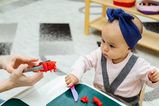 Toddler making shapes with colorful modeling clay or Play-Doh on a table in the kindergarten