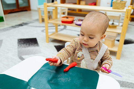 Closeup of toddler making shapes with colorful modeling clay or Play-Doh on a table in the kindergarten