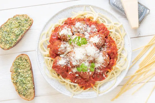 Homemade beef meatballs in tomato sauce with italian bucatini pasta, grated parmesan and fresh cilantro in a grey plate with garlic bread