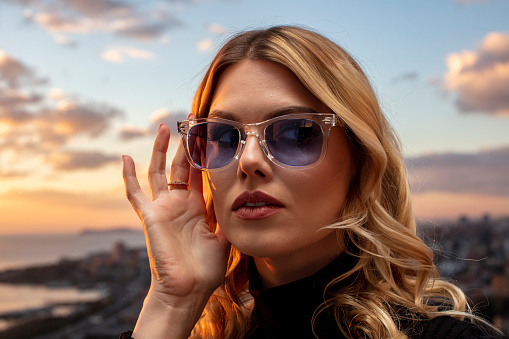 Beautiful female model wearing colorful glasses at sunset. Outdoors romantic portrait of attractive blonde woman with makeup and glasses posing. Istanbul archipelago (Princess Islands) skyline.