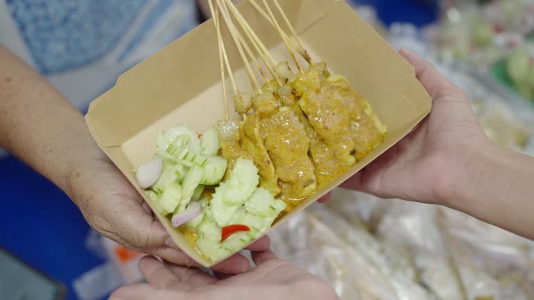 Pork satay topped with sauce and given to Asian woman