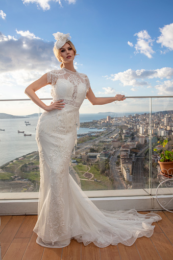 Beautiful female model in a wedding dress. Outdoors romantic portrait of attractive blonde woman with makeup and wedding hairstyle posing on balcony against Istanbul view.