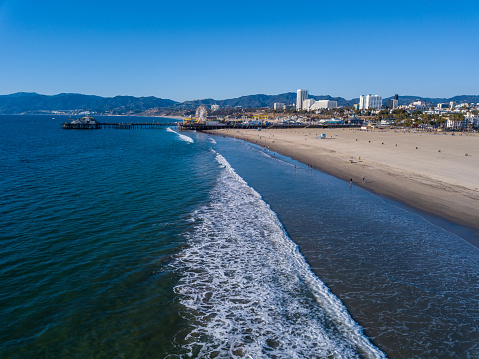 Aerial views of the famous Santa Monica Pier. Birds Eye view photos taken on public beach with a drone. The crowded amusement park sits over the Pacific Ocean on the California coast.