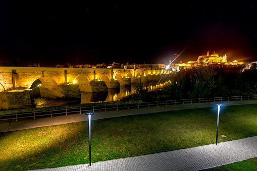 View of the Roman Bridge, a stone bridge that spans the river Guadalquivir in Cordoba, Spain at night.