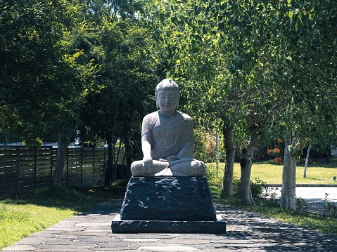 An old stone buddha statue in an urban park on a sunny day surrounded by nature
