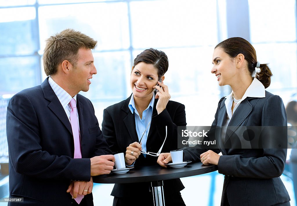 Businesspeople having coffee break Three happy businesspeople standing by coffee table and talking. Mid Adult Men Stock Photo