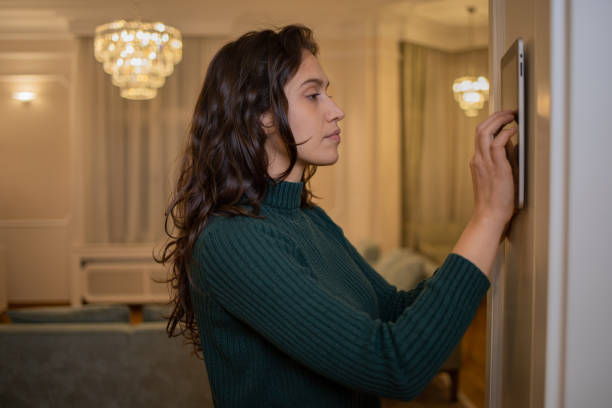 istock Young woman adjusts the temperature at home with a device on the wall 1452380140