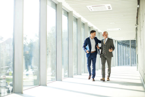 istock Senior and junior management business people walking through hallway and talking 1452382489