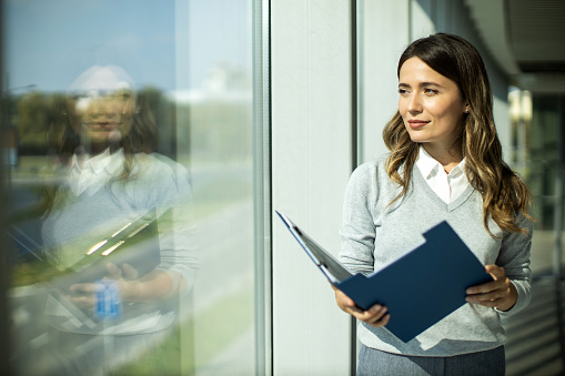 Young adult female businesswoman standing and looking at document in a modern office hallway