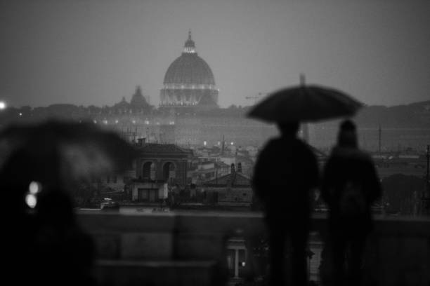 Tourists with umbrellas during a rainy day in Rome, enjoying the view from Pincio to Piazza del Popolo, with domes and cityscape.