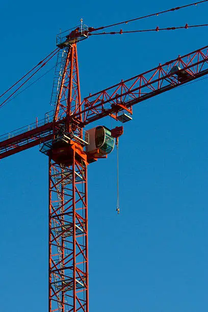 Photo of tower crane showing the operators box and hook set against a plain blue sky.