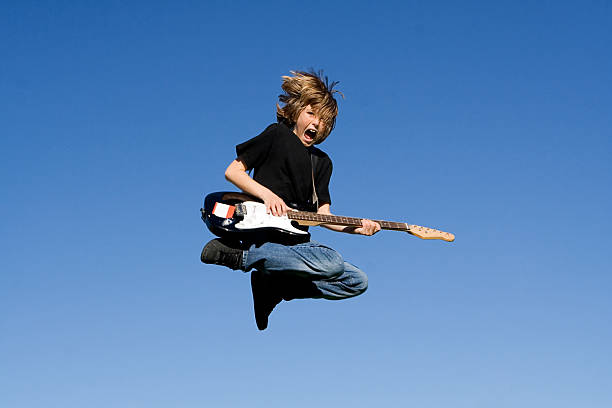 Young boy playing the electric guitar while jumping stock photo